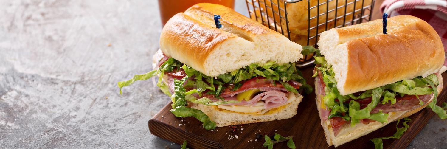 turkey sub sandwich cut in half on a table with chips and a beer behind it